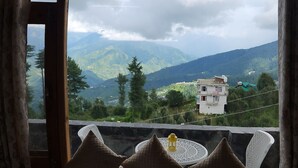 A room with a bed, a window, and a view of mountains.