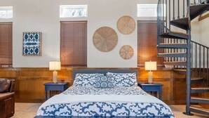 A bedroom with a bed, two nightstands, a blue bench, a spiral staircase, and wall decorations.