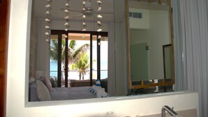 A bedroom with a large bed, a ceiling fan, a mirror, and a view of the beach. - Beachfront apartment in Akumal U3 (Akumal)