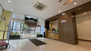 A hotel reception area with a modern design, including a reception desk, a waiting area, and a visible outdoor view through large windows. - One Palm Tree Villas (Pasay)