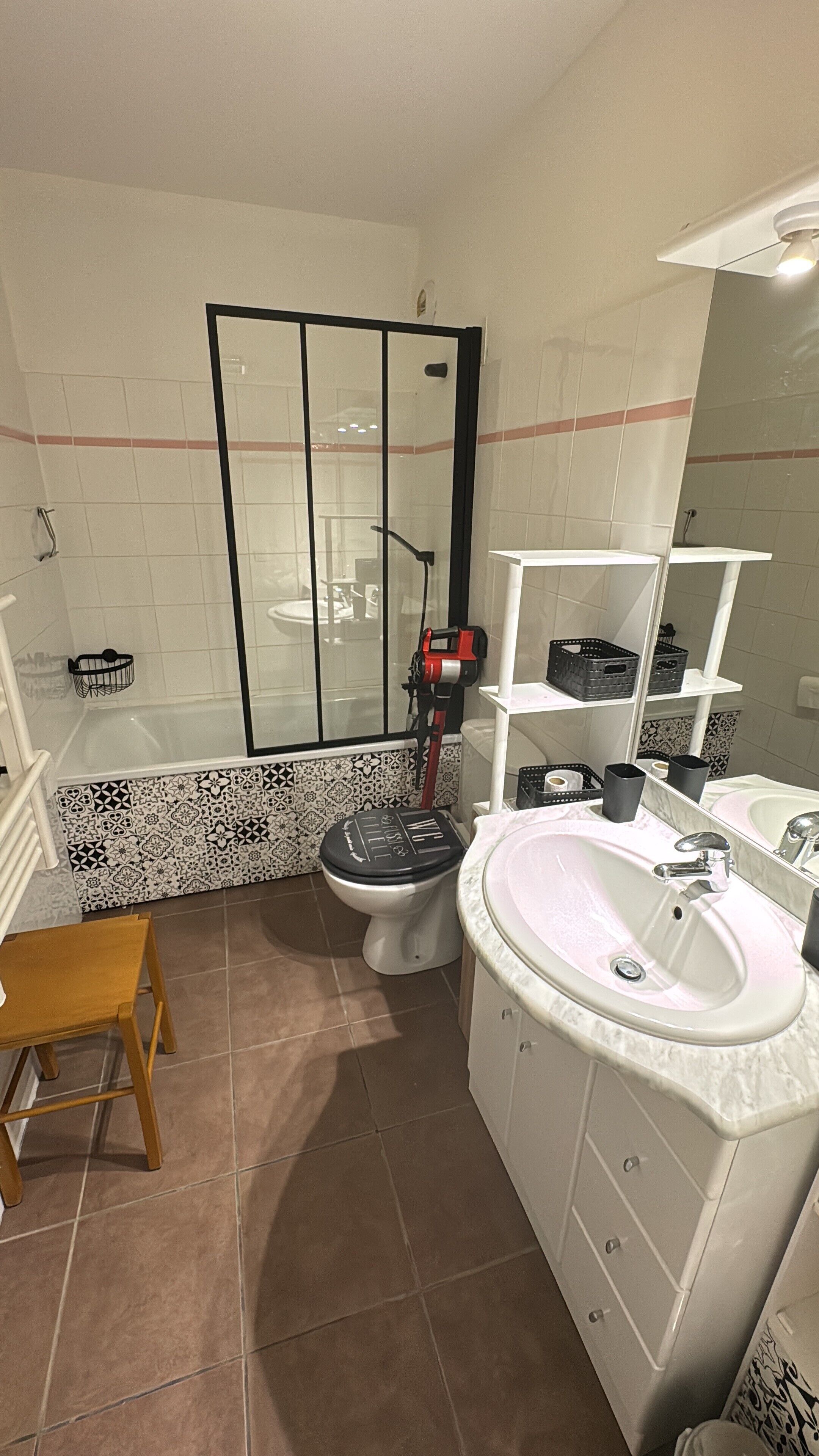 A bathroom with a shower, toilet, sink, and a wooden stool.