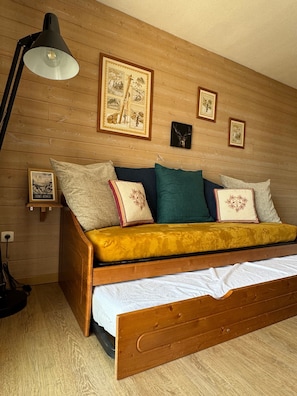 A wooden bed with a yellow blanket, a bedside lamp, and framed pictures on the wall.