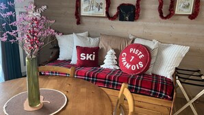 Ein gemütliches Zimmer mit einem karoüberzogenen Sofa, einem kleinen Weihnachtsbaum und einem Tisch mit einer Vase.