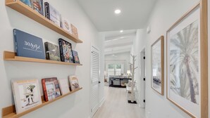 A hallway with wooden shelves displaying books, a white door, and a framed picture on the right. - The Modern Cottage near 30a, Golf Cart + Bikes included! (Inlet Beach)