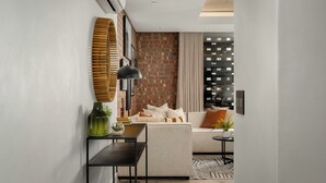A modern living room with a sofa, a coffee table, and a side table. There is a brick wall and a window with curtains. - The Signature | Lush Designer Apartment (Cape Town)