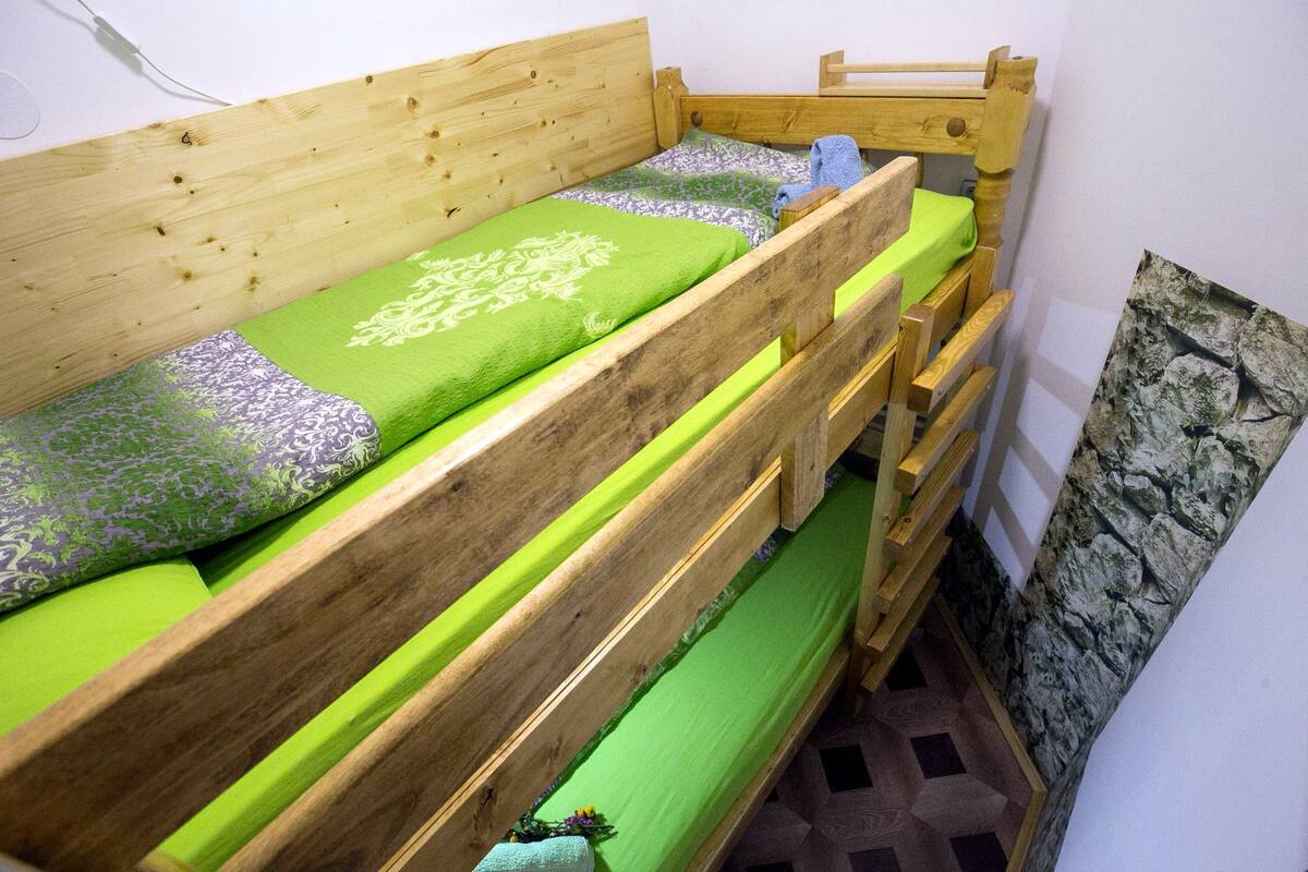 Ein Etagenbett mit grüner Bettwäsche und einem gemusterten Kopfkissen.