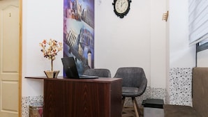 A reception area with a wooden desk, a laptop, a chair, a red rug, a clock, and a wall with a cityscape poster. - Hostel Put Svile-Hostel Silk Road (Subotica)