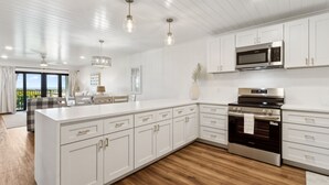 A modern kitchen with white cabinetry, stainless steel appliances, and a wooden floor.