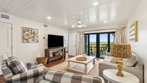 A living room with a sofa, a coffee table, a TV, and a view of the outdoors.