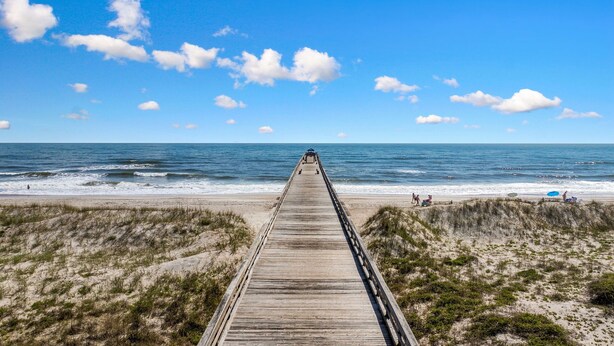 A wooden boardwalk leading to a beach with dunes and the ocean in the background.