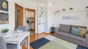 A modern living room with a grey sofa, a dining table with chairs, and a kitchen in the background. - Liiiving in Gaia - Douro Balcony View (Vila Nova de Gaia)