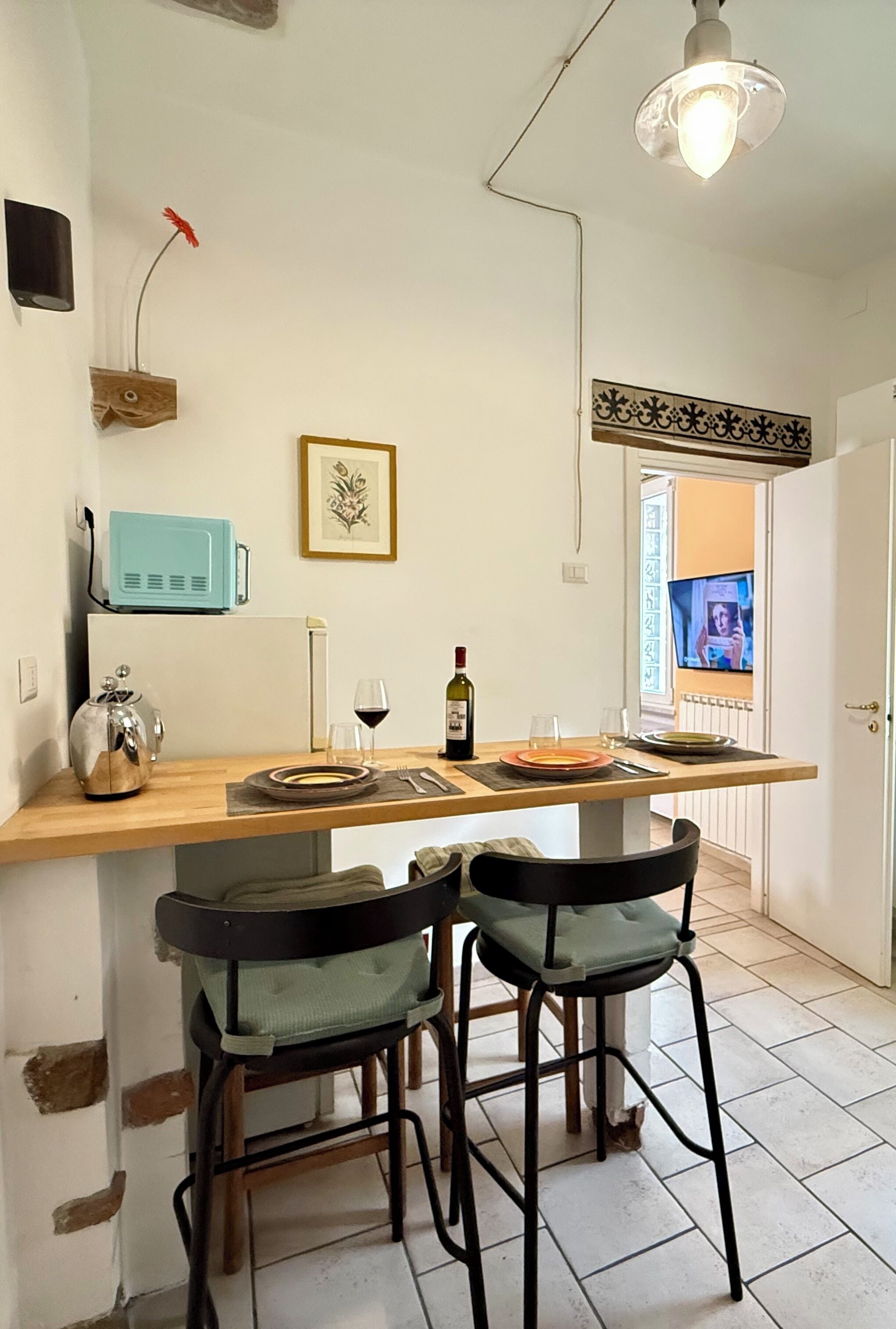 A kitchen with a wooden island, two bar stools, a small refrigerator, and a television in the background.