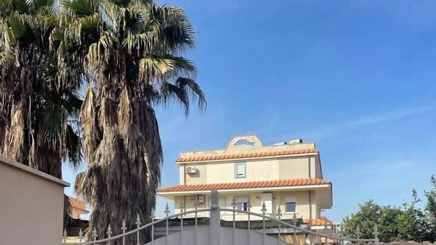 Una entrada portonada con un camino de losas de piedra que conduce a un edificio con tejado de tejas y un balcón.