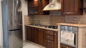 Una cocina con refrigerador de acero inoxidable, estufa a gas, armarios de madera y salpicadero de azulejos.