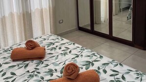 Habitación de hotel con cama, dos toallas enrolladas, un espejo grande y una puerta corrediza que da a un baño.