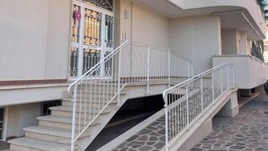 Un edificio de varios pisos con entrada empedrada en piedra y barandillas blancas.