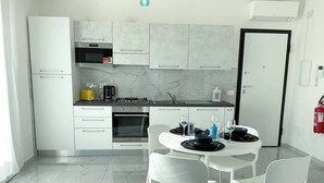 A modern kitchen with white cabinets, a built-in oven, and a dining area with a round table and white chairs. - House on the Beach, House on the beach near the airport (Isola Sacra)