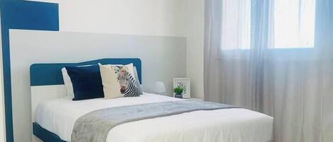 A modern bedroom with a bed, a nightstand, and a window with curtains.