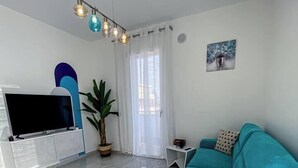 A modern living room with a teal sofa, a flat-screen TV, a potted plant, and a painting on the wall. - House on the Beach, House on the beach near the airport (Isola Sacra)
