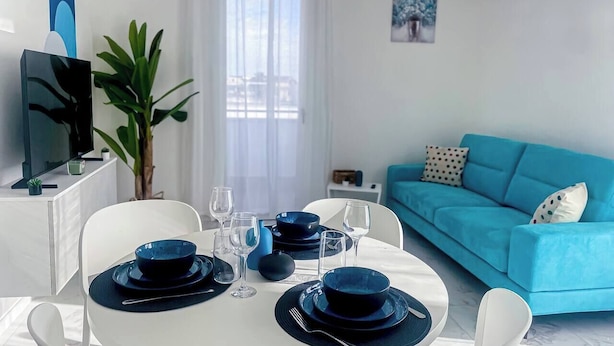 A dining area with a round table set for four, white chairs, and a blue sofa in the background. - House on the Beach, House on the beach near the airport (Isola Sacra)