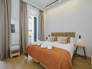 Una habitación de hotel moderna con una cama grande, una mesita de noche, un espejo y vistas al balcón exterior.