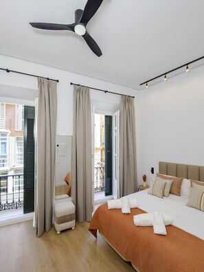 Habitación de hotel con cama, cortinas, ventilador de techo y vistas al exterior.