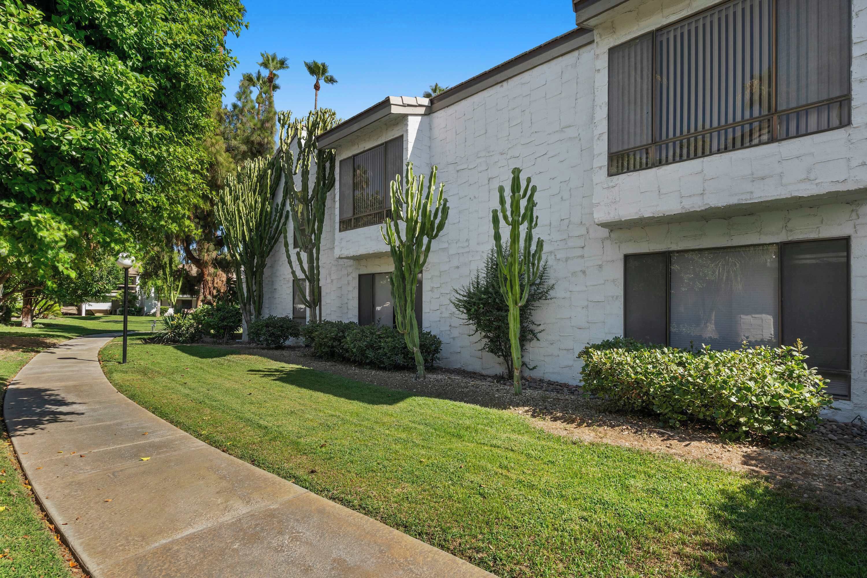 A modern building with a concrete pathway, cacti, and well-maintained grass.