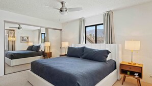 Ein Schlafzimmer mit einem großen Bett, einem Deckenventilator, einem Nachttisch mit Lampe und einem Fenster mit Vorhängen.