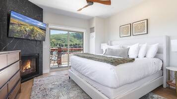 A bedroom with a large bed, a fireplace, a ceiling fan, and a balcony with a mountain view.