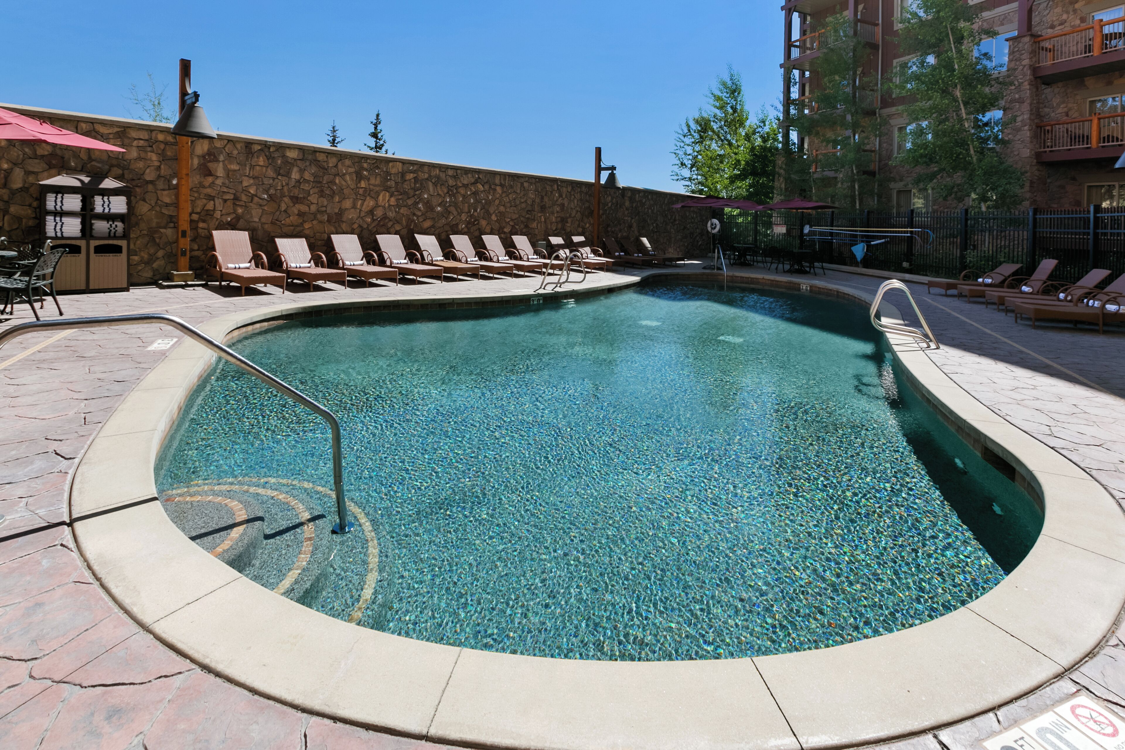 Una piscina con sillas de descanso y un muro de piedra.