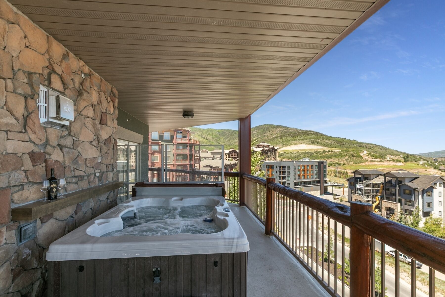 A hot tub on a balcony with stone walls and a view of buildings and hills.