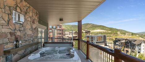 A hot tub on a balcony with stone walls and a view of buildings and hills.
