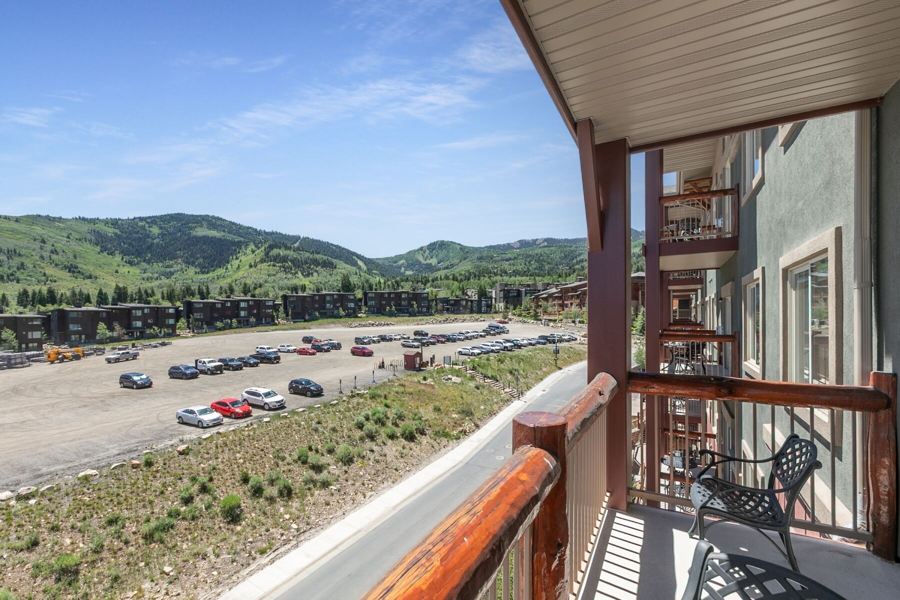 Une vue d’un parking rempli de voitures, d’un immeuble doté de balcons et, au loin, d’un paysage montagneux.