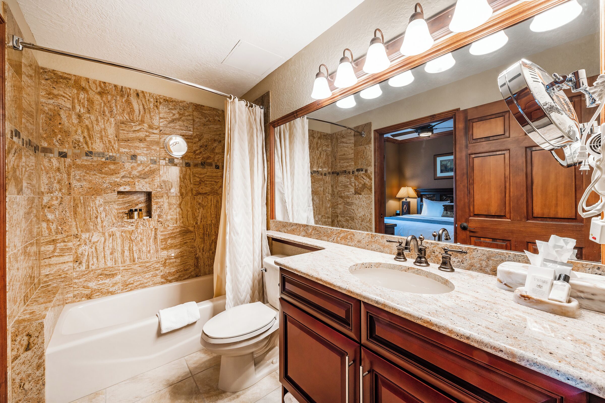 Un baño con bañera, inodoro, tocador con lavabo y un espejo grande.