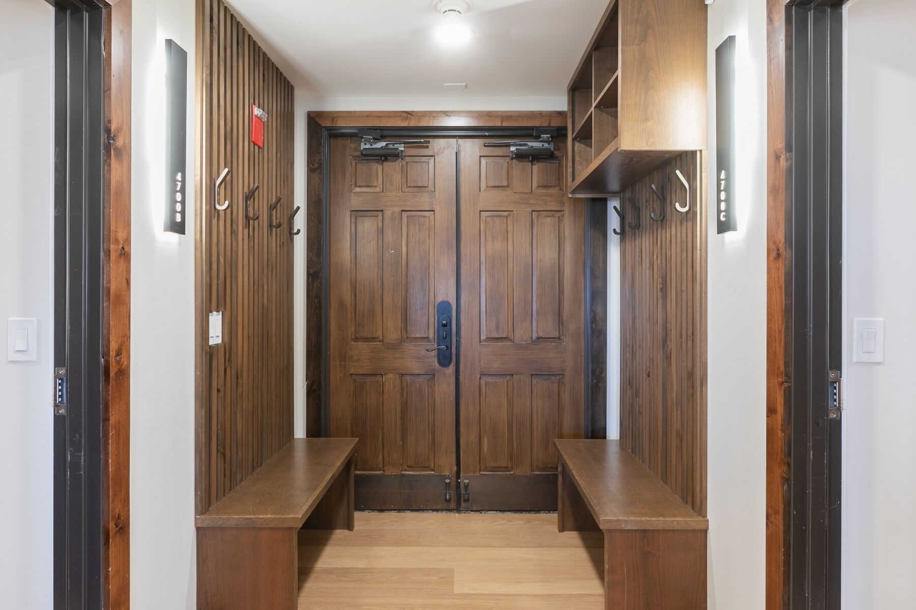 Un pasillo con puertas dobles de madera, un banco y una lámpara en el techo.