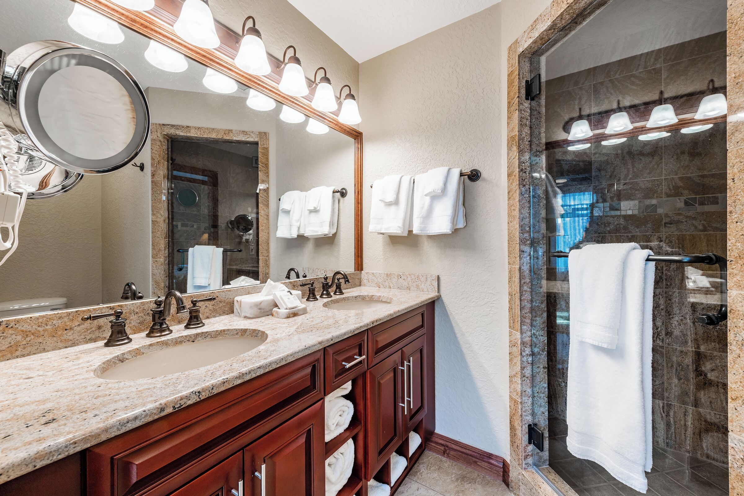 A bathroom with a granite countertop, a large mirror, and a glass-enclosed shower area.
