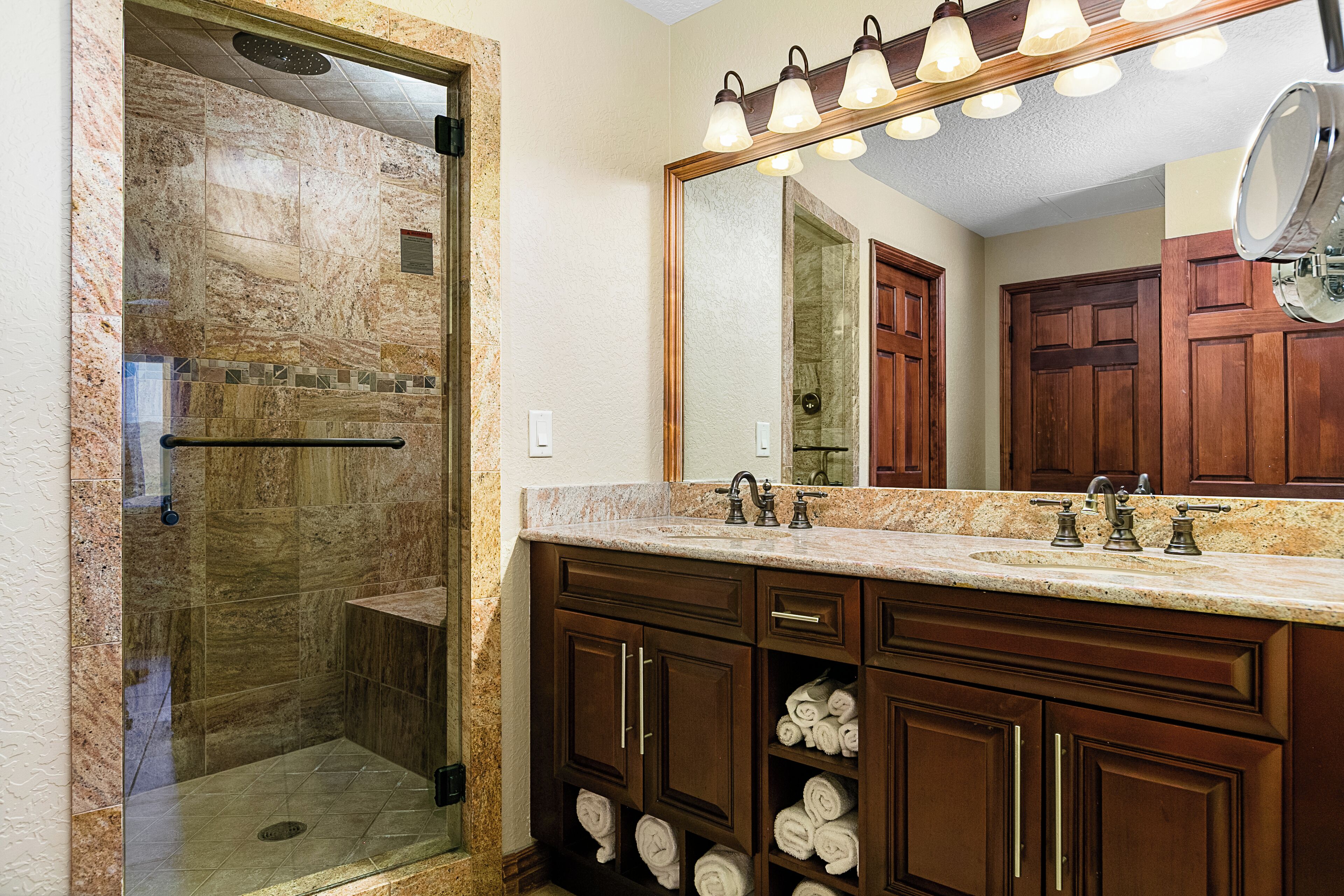 A bathroom with a glass-enclosed shower, a vanity with a sink, and a large mirror above the vanity.