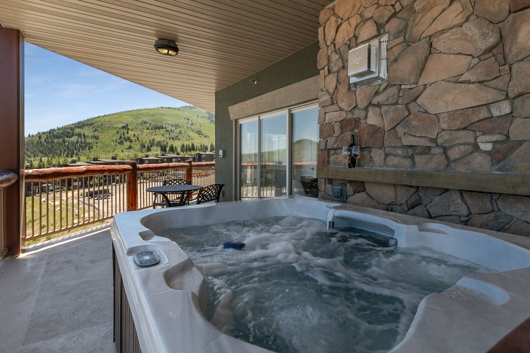 Un jacuzzi en un balcón con una pared de piedra y vistas a la montaña.