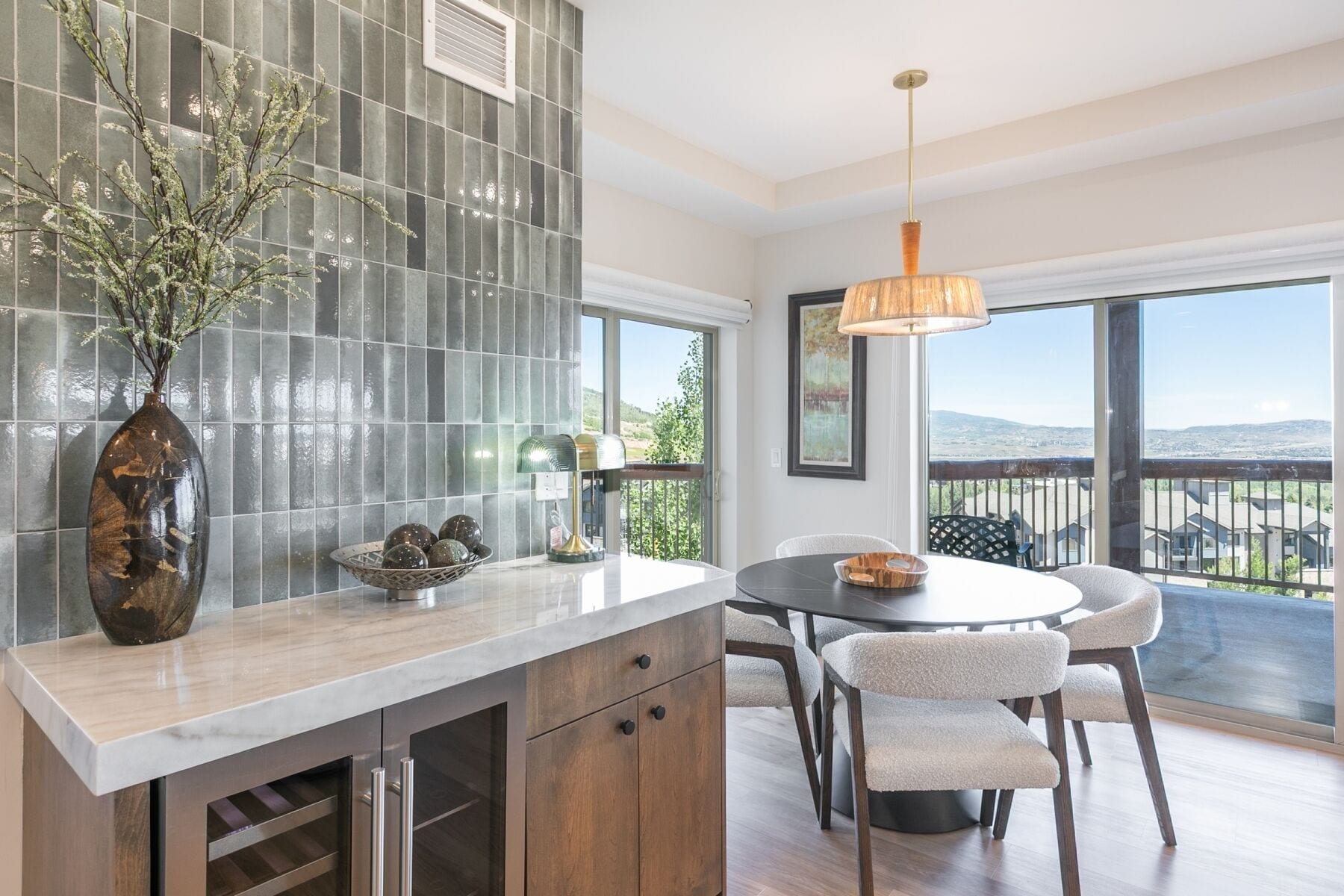 A modern kitchen with a large island, a dining area with chairs, and a view of the outdoors through large windows.