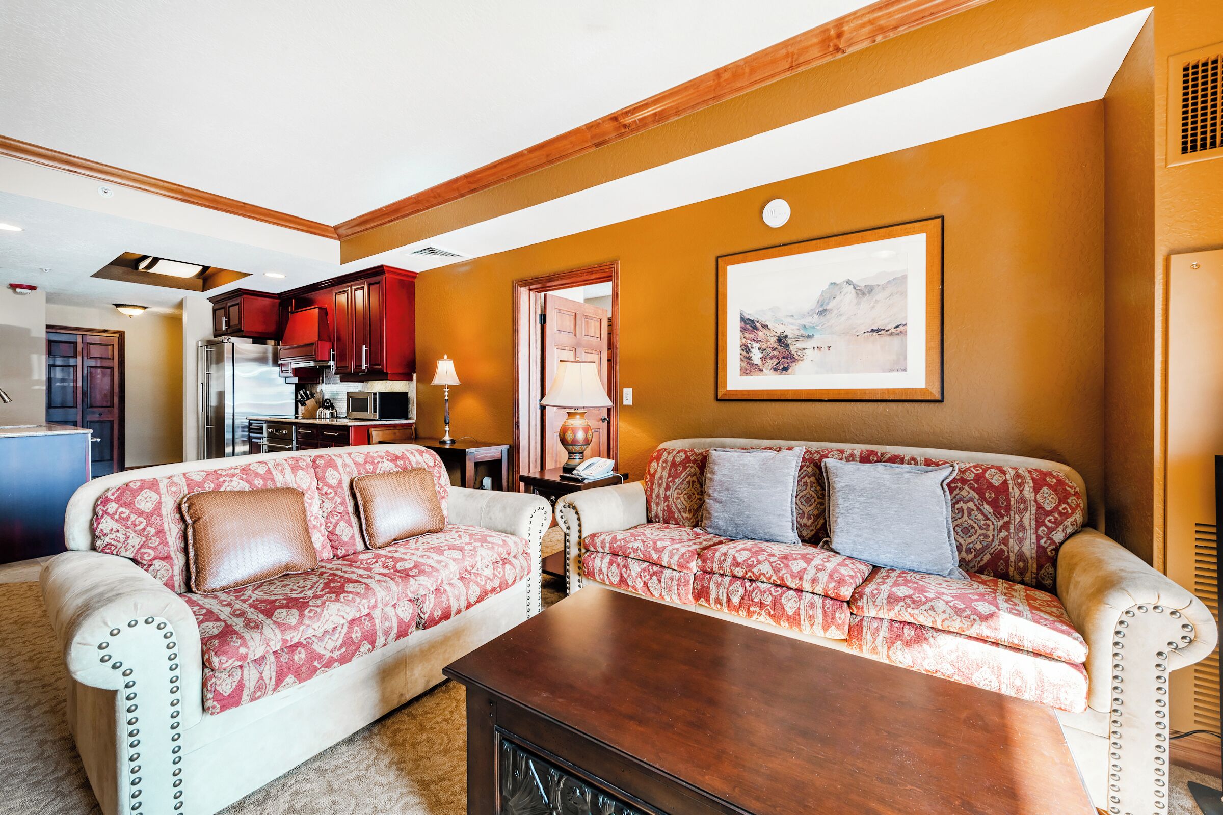 A living room with two patterned sofas, a wooden coffee table, and a kitchen in the background.