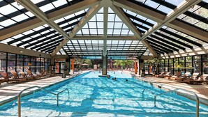 Una piscina interior con techo de cristal, rodeada de sillas de descanso y suelo de baldosas.