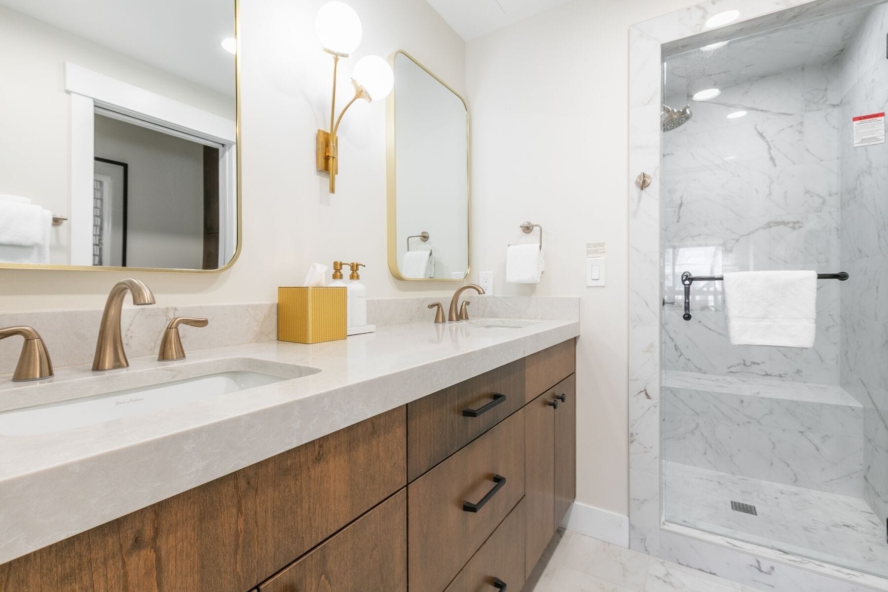 Un baño moderno con dos lavamanos, un espejo, ducha y muebles de madera.