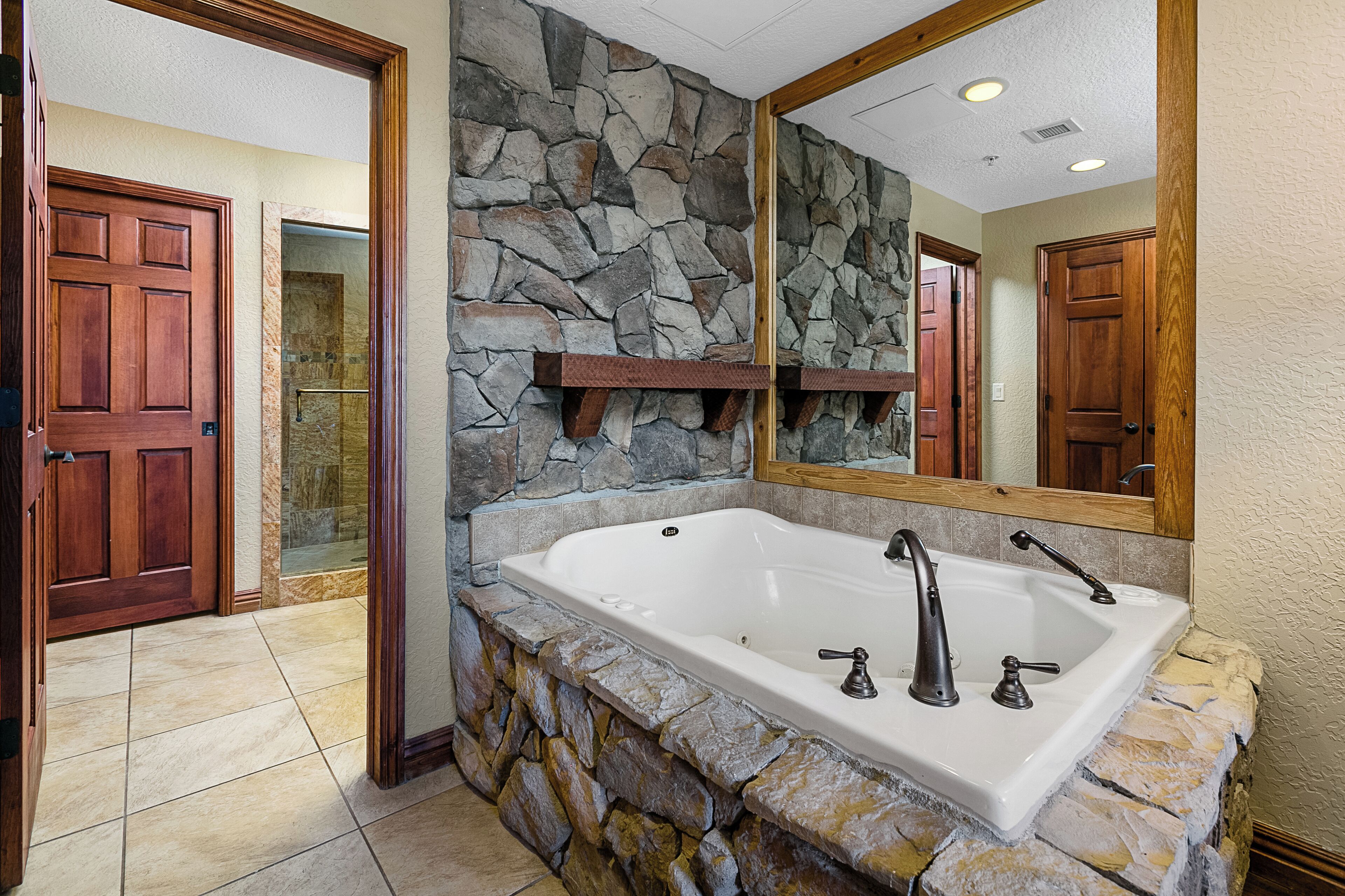 Un baño con pared de piedra, una bañera grande y puertas de madera.