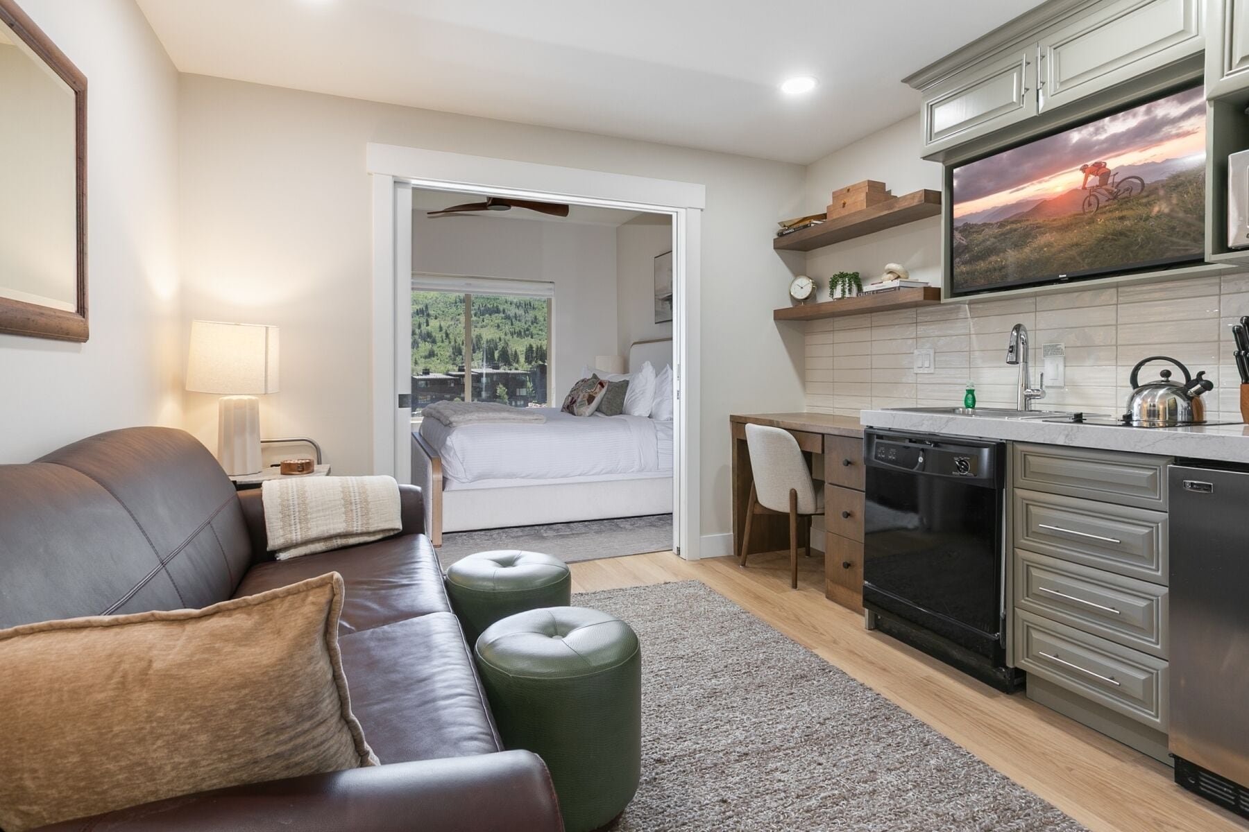 A modern hotel room with a bed, a sofa, a dining area, and a kitchen.