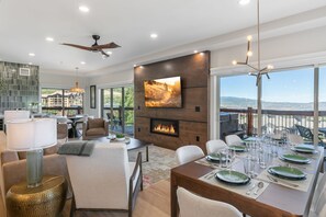 A modern living room with a fireplace, dining area, and large windows overlooking a scenic view. - Condos at Canyons Resort by White Pines (Park City)