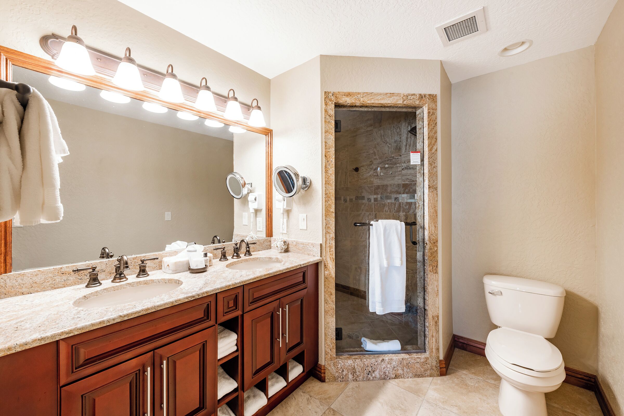 A bathroom with a double sink vanity, a large mirror, and a glass-enclosed shower stall.