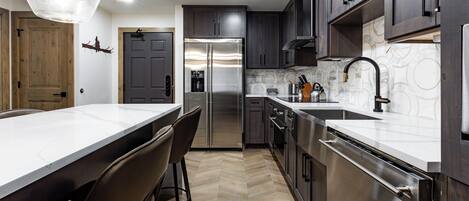 A modern kitchen with a large island, dark wooden cabinets, stainless steel appliances, and a herringbone floor pattern.