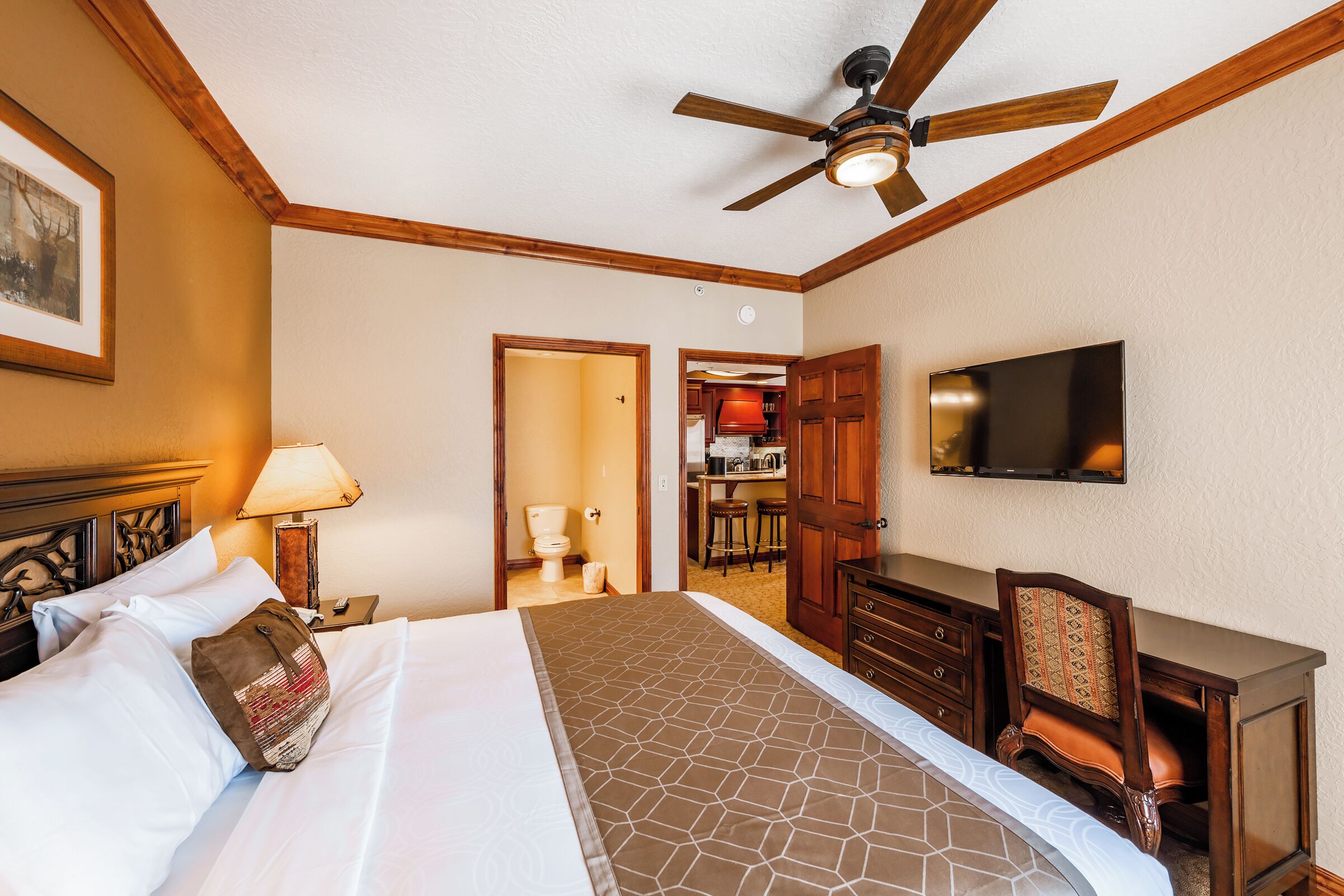 Ein Hotelzimmer mit Bett, Schreibtisch, Stuhl, Fernseher und Deckenventilator.