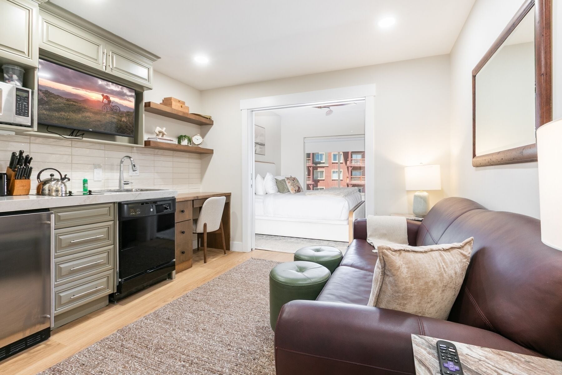 Eine moderne Wohnung mit Küche, einem Wohnbereich inklusive Sofa und Poufs, einem Bett sowie Blick auf Gebäude.