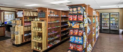 A grocery store interior with wooden shelves stocked with snacks, a refrigerated display case, and a checkout counter.